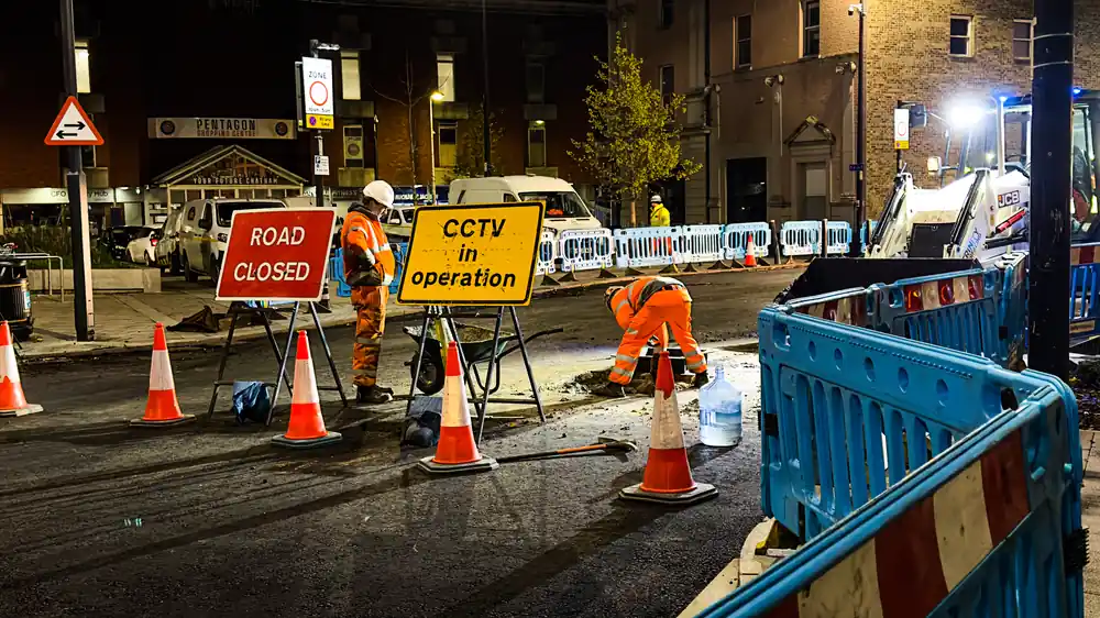 Two road workers in orange high-visibility clothing at work behind cones and a Road closed sign on Globe Lane, Chatham, at 22:04
