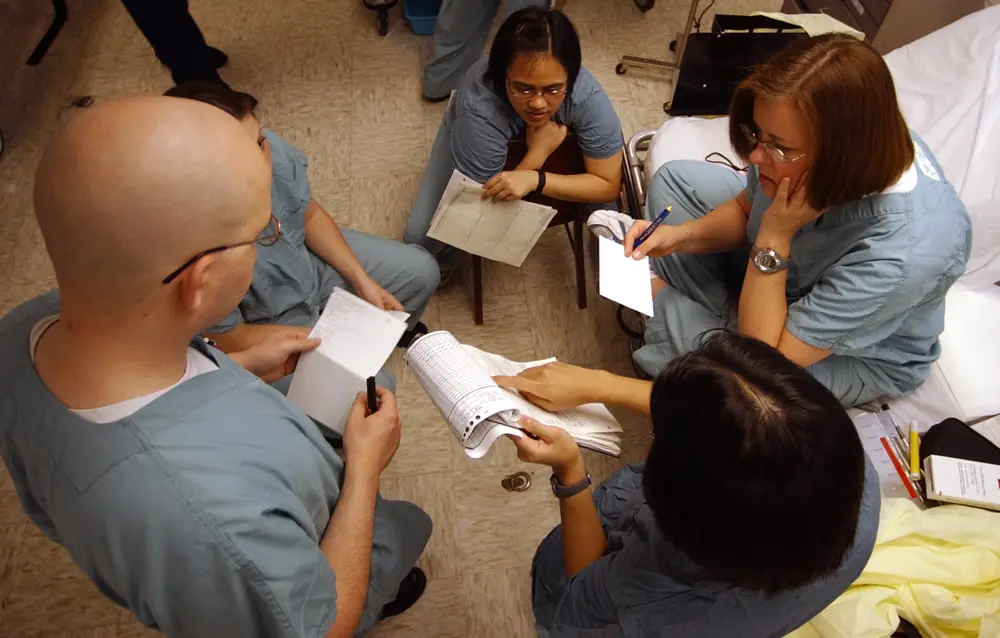 Intensive care staff in scrubs sit in a circle reading patient notes before taking over for the night aboard the hospital ship USNS Comfort