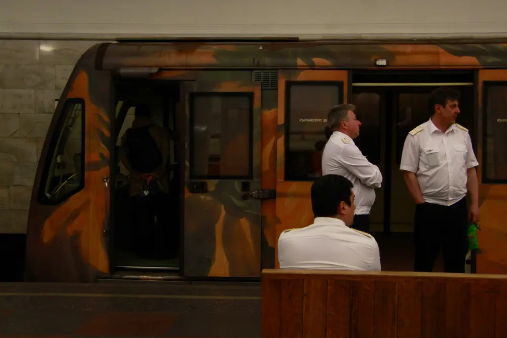 Three metro drivers in white uniform shirts wait beside a train at Kropotkinskaya station, Moscow, at 03:24